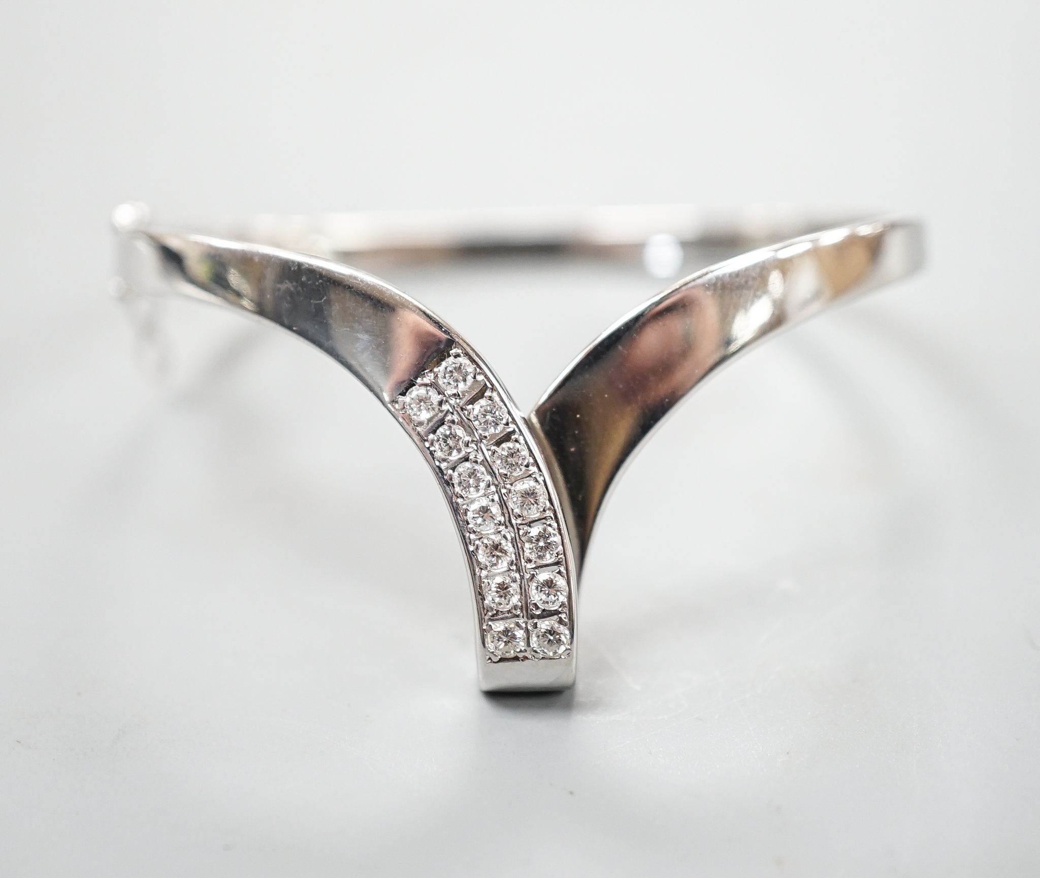A modern 585 white metal and twelve stone diamond set wishbone shaped hinged bangle, gross 19.7 grams.